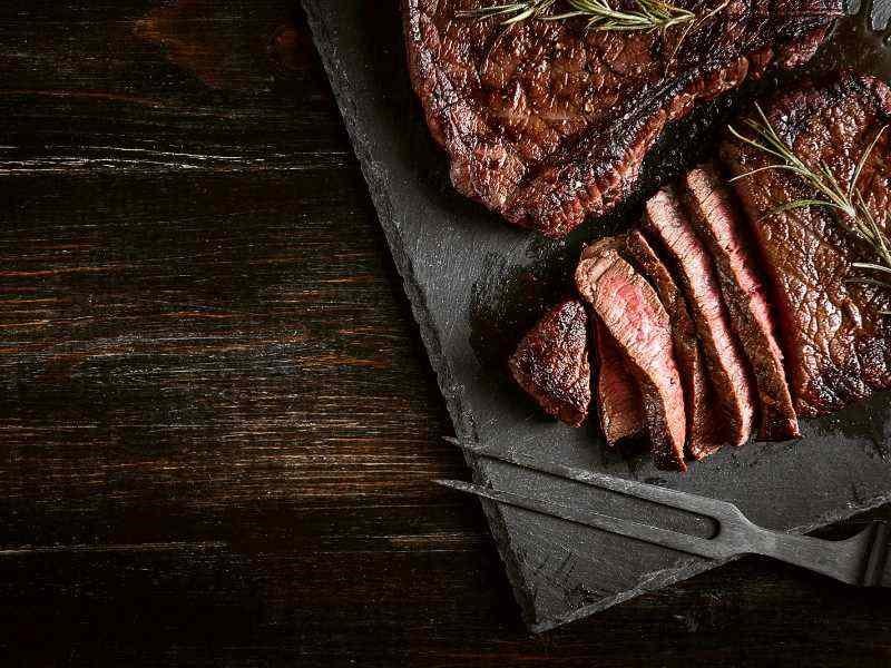 A sliced steak on a slate plate with a knife and fork.