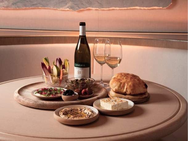 A table setting with a bottle of wine, two glasses, bread, cheese, and various dishes.