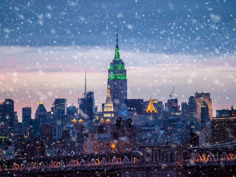a snowy cityscape at dusk with a prominent skyscraper in the center